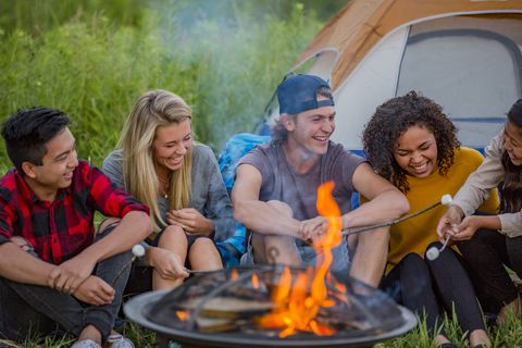 teenage friends roasting marshmallows over a campfire and laughing