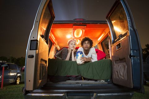 couple holding popcorn while sitting in camping van during drive in movie