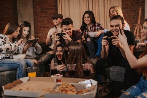 a big rowdy group of teens playing video games and eating pizza