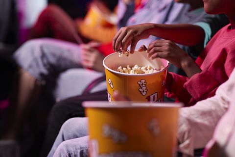 midsection of friends sharing popcorn while sitting in theater