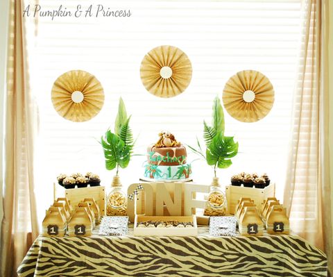 A first birthday party with a safari or jungle theme includes an animal print tablecloth, fake greenery and a jungle-themed cake a first birthday party with a safari or jungle theme includes an animal print tablecloth, fake greenery and a jungle themed cake
